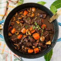 square image of beef bourguignon in a large pot with a sprig of thyme for garnish