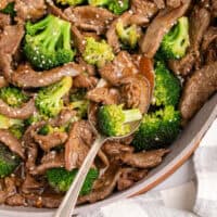 skillet of beef and broccoli with a serving spoon with recipe name at the bottom