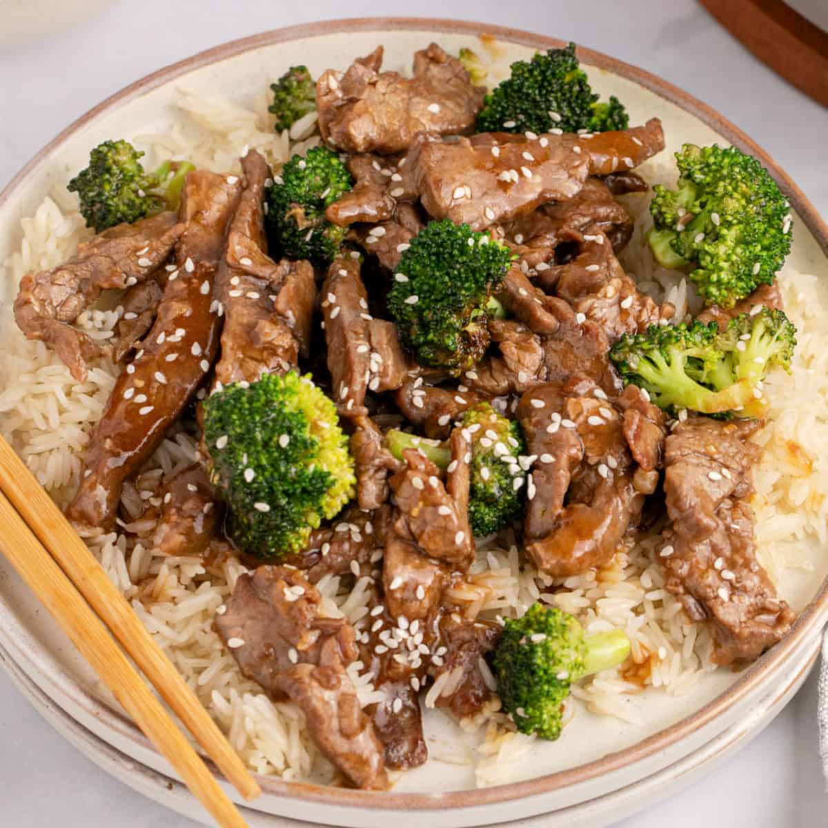 square image of beef and broccoli served over cooked white rice with chopsticks
