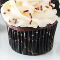 close up of a chocolate cupcakes with cream cheese frosting and sprinkles with recipe name at the bottom