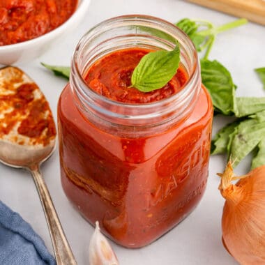 square image of best ever pizza sauce in a mason jar with a basil leave on top