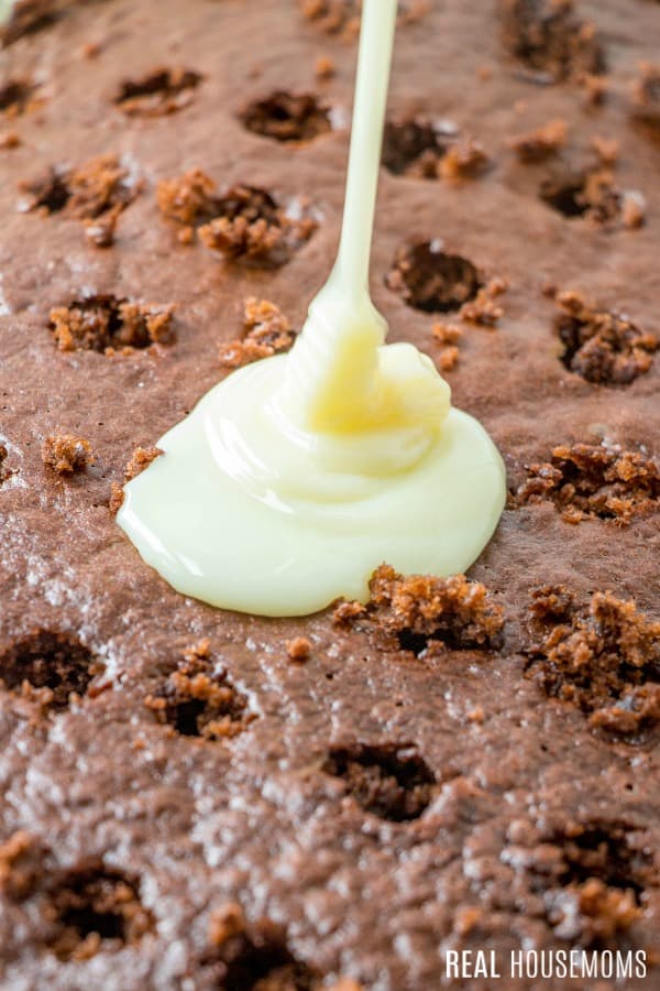 sweetened condensed milk being poured over chocolate poke cake