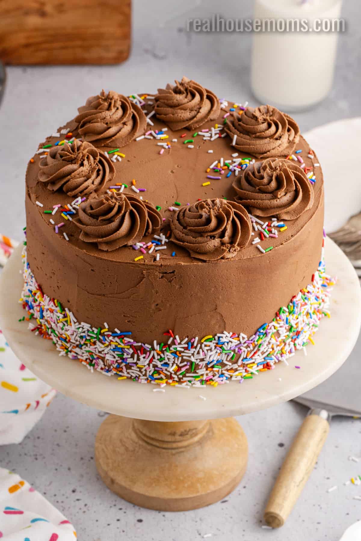 frosted birthday cake with rosettes on top and sprinkles around the bottom edge on a cake stand