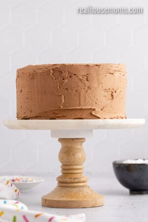 crumb coated birthday cake on a cake stand before chilling