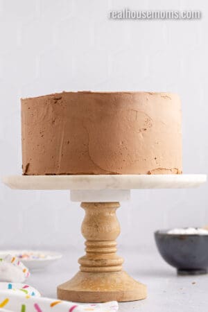 chocolate frosted birthday cake on a cake stand after chilling in the fridge