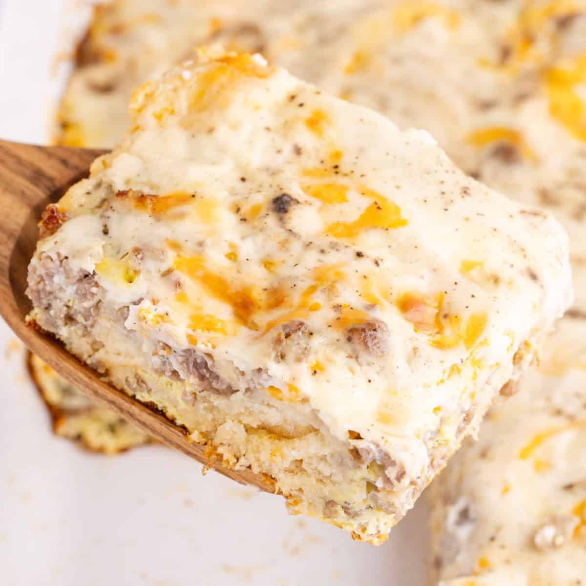 square image of biscuits and gravy breakfast casserole on a wooden spatula over the baking dish