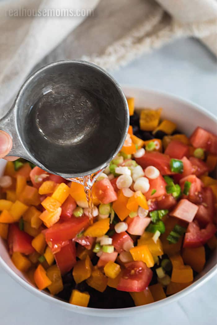 white wine vinegar being added to a bowl for black bean salad
