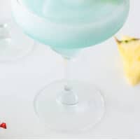 blue margarita in a margarita glass garnished with cherry and pineapple with recipe name at the bottom