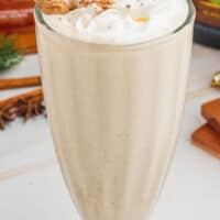 image of a boozy eggnog milkshake topped with whipped crema and nutmeg title of the post on top of the image in green and black lettering