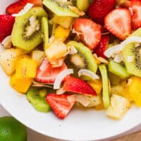 boozy tropical fruit salad in a white serving bowl with recipe name at the bottom