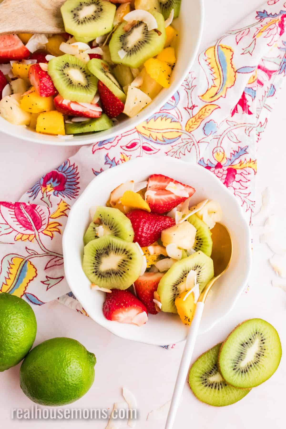 small bowl of boozy tropical fruit salad with a spoon next to the serving bowl and a couple of lime