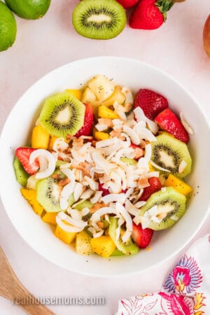 toasted coconut flakes add to a bowl of boozy tropical fruit salad tossed in coconut lime dressing