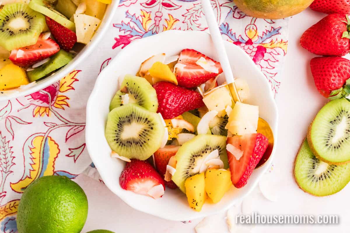 portion of boozy tropical fruit salad in a white bowl with a spoon