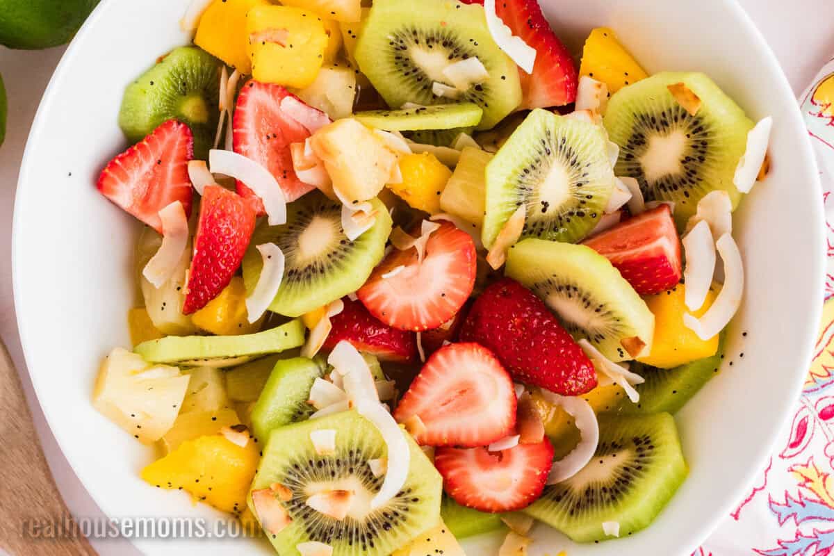 close up of a serving bowl of boozy tropical fruit salad topped with toasted coconut