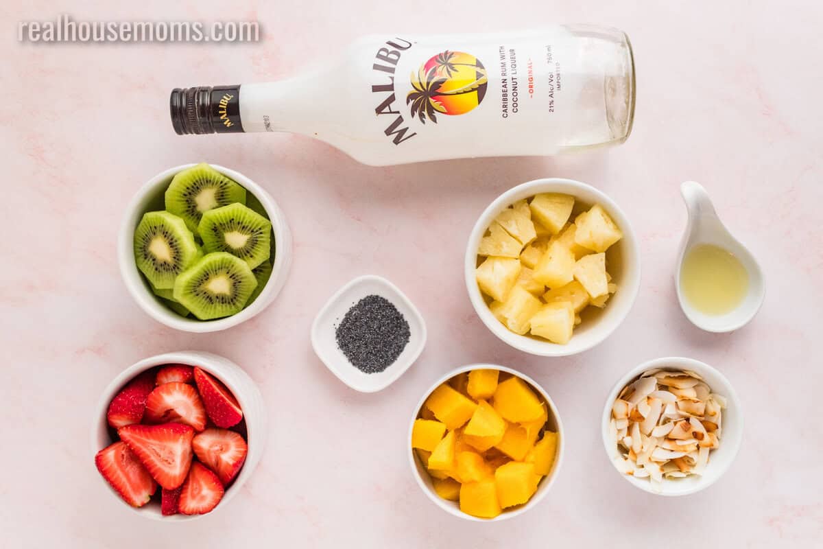 ingredients to make boozy tropical fruit salad in bowls on a counter