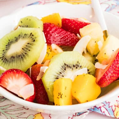 square image of a bowl of boozy tropical fruit salad with a spoon