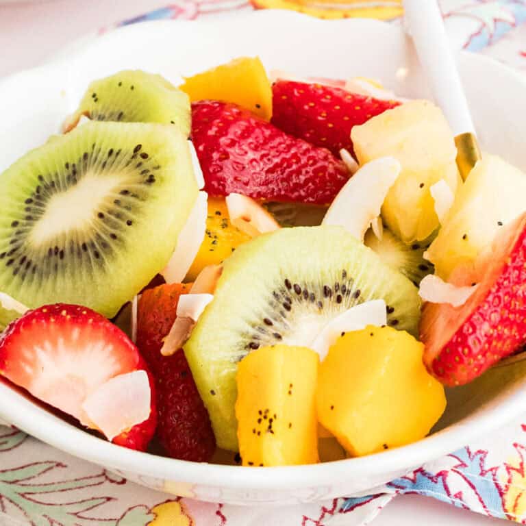 square image of a bowl of boozy tropical fruit salad with a spoon