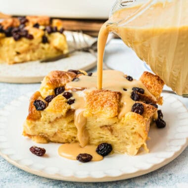 square image of vanilla caramel sauce being poured over a slice of bread pudding with raisins on a plate