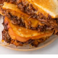 brisket grilled cheese halves stacked up on a plate with recipe name at the bottom
