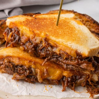 square image of two brisket grilled cheese halves stacked on a plate with a toothpick in the top