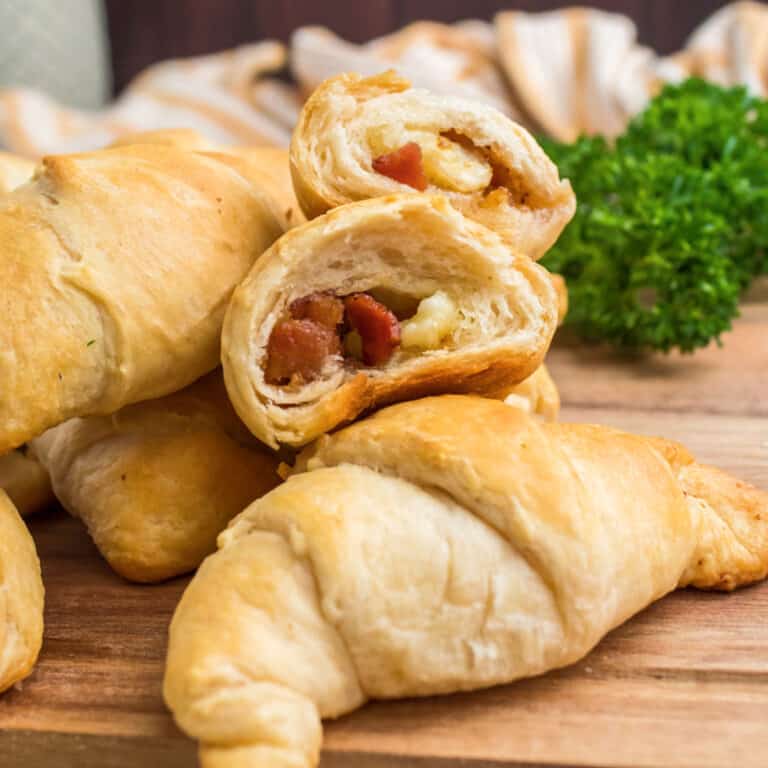 square image of a broken open brown sugar, bacon & brie crescent rolls on a pile of rolls