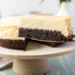 square image of a brownie bottom cheesecake slice on a cake serve in front of the rest of the cake