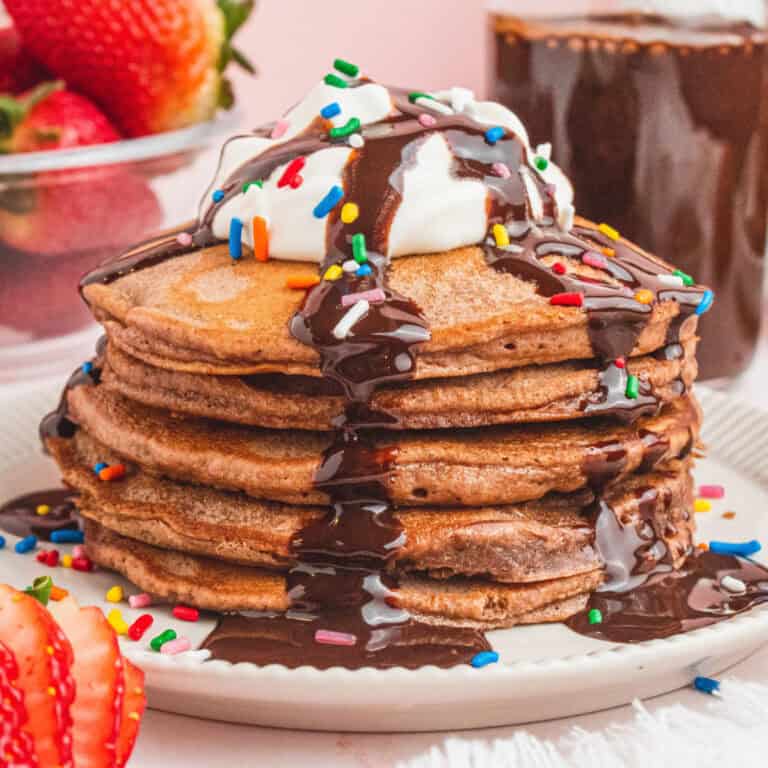 square image of brownie pancakes with whipped cream, chocolate sauce, and sprinkles