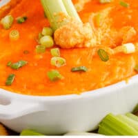 celery sticks being dipped into buffalo cauliflower dip with recipe name at the bottom