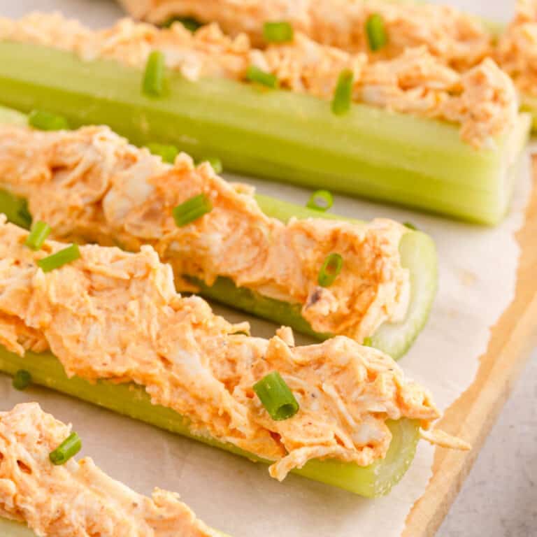 square image of buffalo chicken celery sticks topped with chives on a cutting board