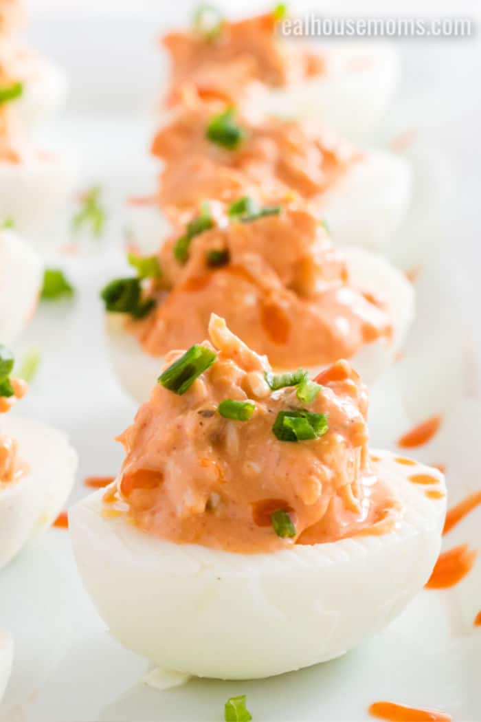 deviled eggs with buffalo chicken filling topped with green onion and hot sauce