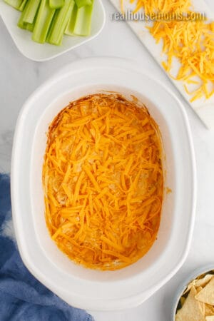 shredded cheddar cheese sprinkled over buffalo chicken dip in the crock pot