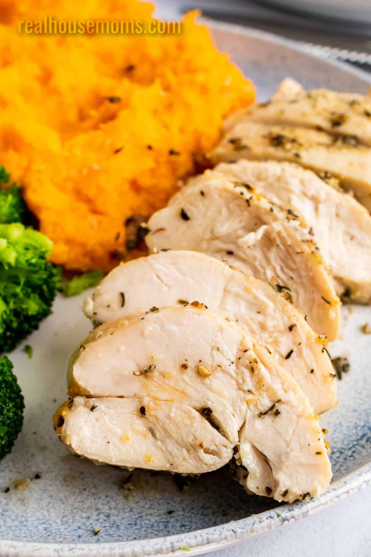 sliced baked chicken breast on a plate with mashed sweet potatoes and borccoli