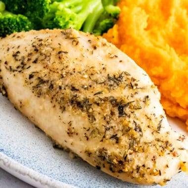 square image of baked chicken breast on a dinner plate with sides