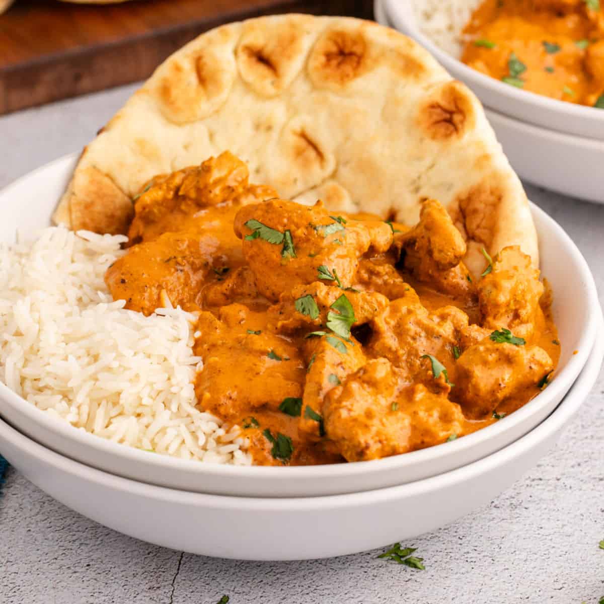 square image of butter chicken with cooked rice and naan bread in a bowl