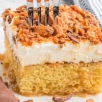 square image of butterfinger cake on a plate with a fork stuck into the top