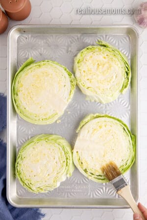 garlic butter being brushed on green cabbage slices on a baking sheet
