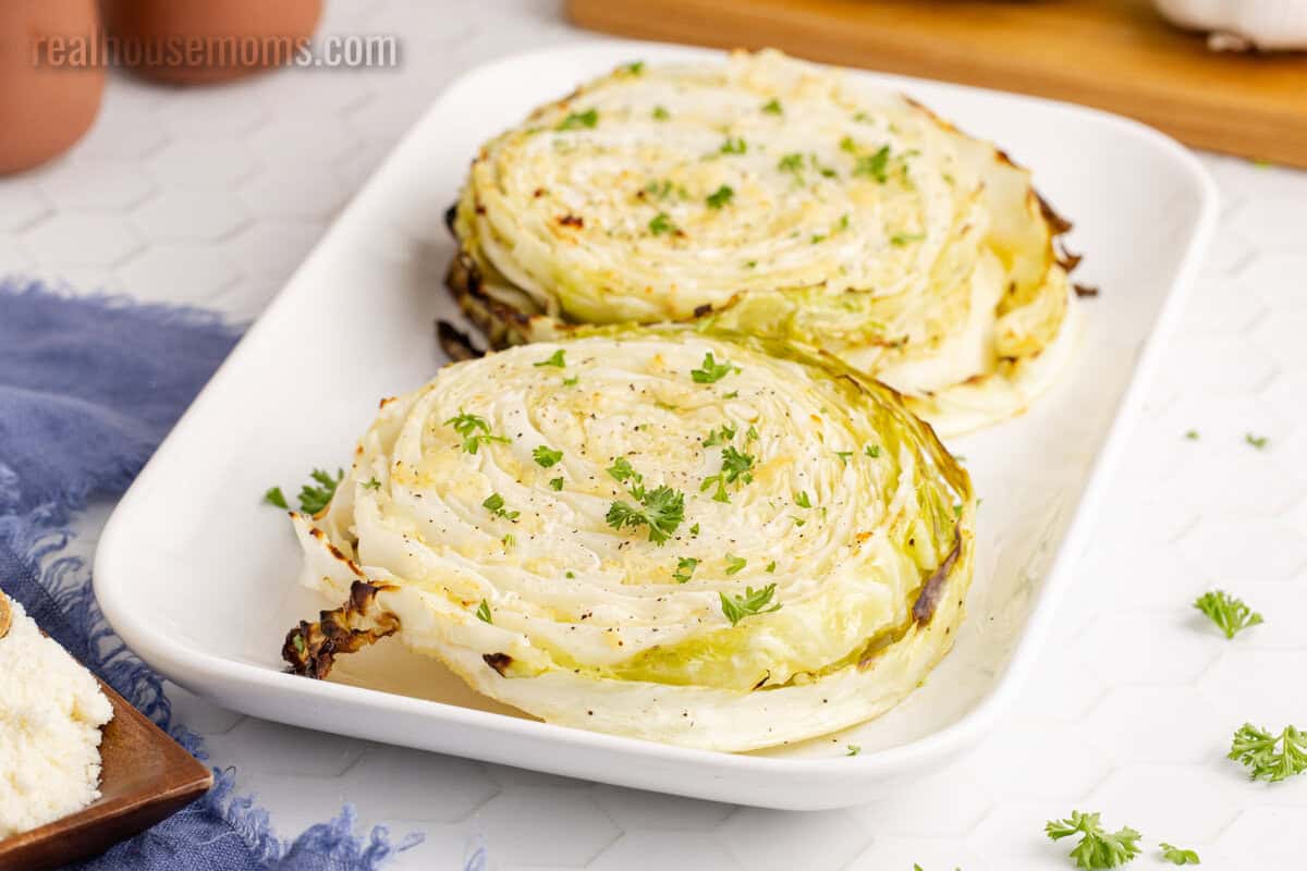 two cabbage steaks topped with parmesan and parsley on a white platter