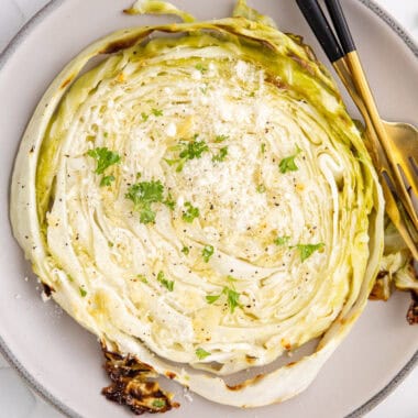 square image of a roasted cabbage steak topped with parmesan and parsley