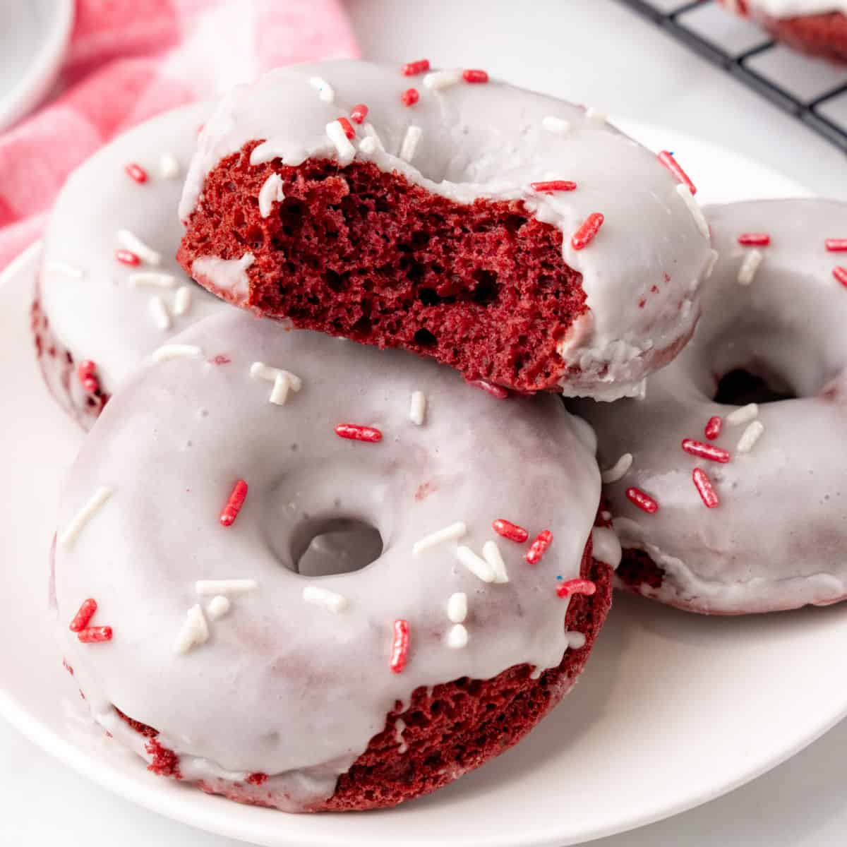 square image of cake mix red velvet donuts piled on a plate with a bite taken out of one to show the donut texture