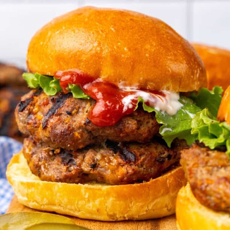 square image of a campfire cheesy bbq burger on a wooden board