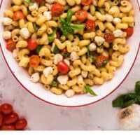 caprese pasta salad in a serving bowl with a wooden spoon with recipe name at the bottom