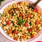 square image of caprese pasta salad in a serving bowl with a wooden spoon