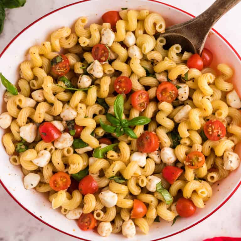 square image of caprese pasta salad in a serving bowl with a wooden spoon