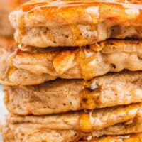 close up image of a stack of carrot cake pancakes topped with syrup and walnuts on a plate with the title of hte post on top of th eimage in blue and black lettering