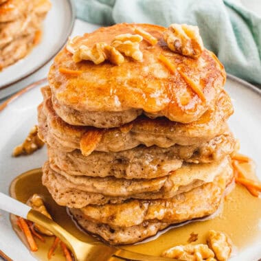 square image of a stack of carrot cake pancakes topped with syrup and walnuts on a plate