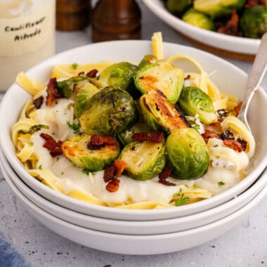square image of fettuccine topped with cauliflower alfredo sauce, bacon, and brussels sprouts