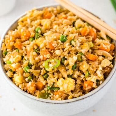 square image of cauliflower fried rice in a bowl with chopsticks on the rim