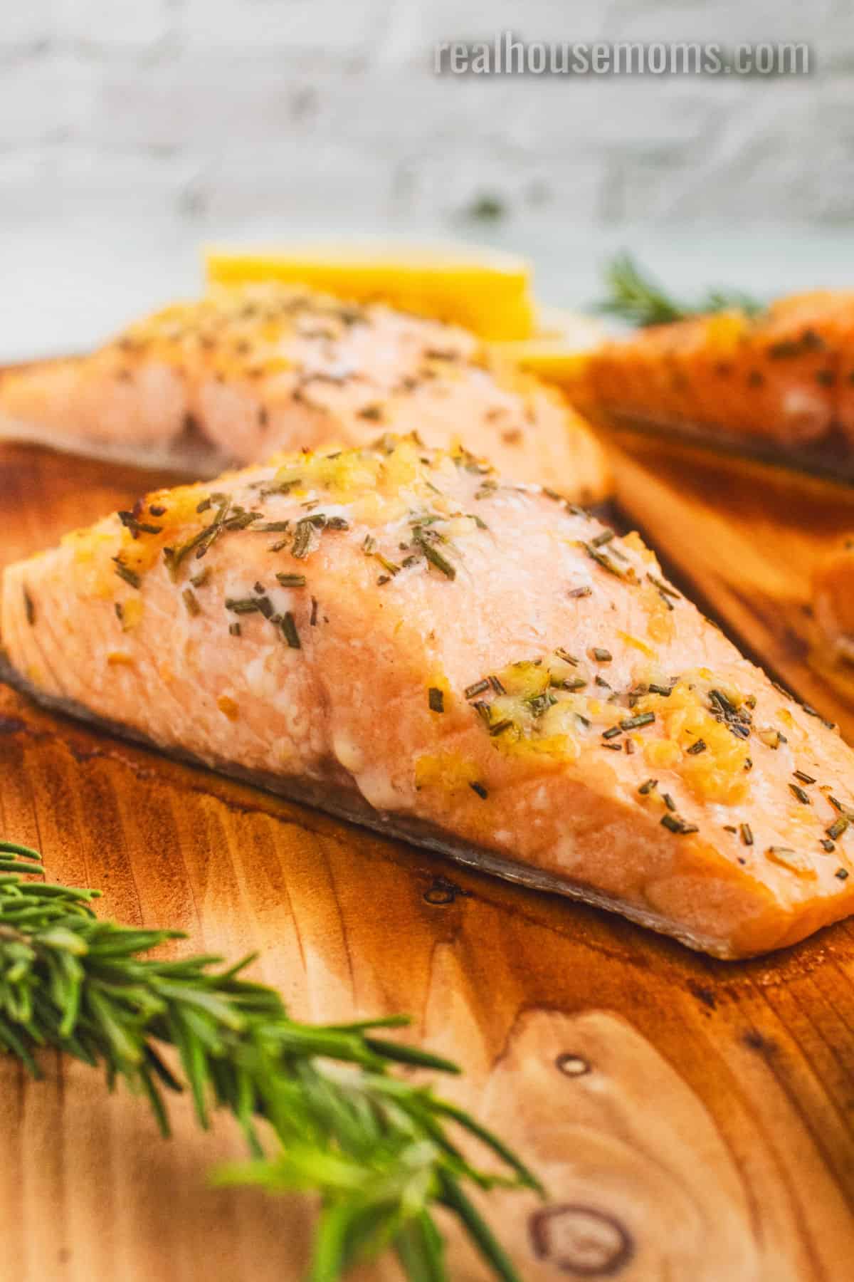side view of cedar plank salmon on the plank with a sprig of fresh rosemary