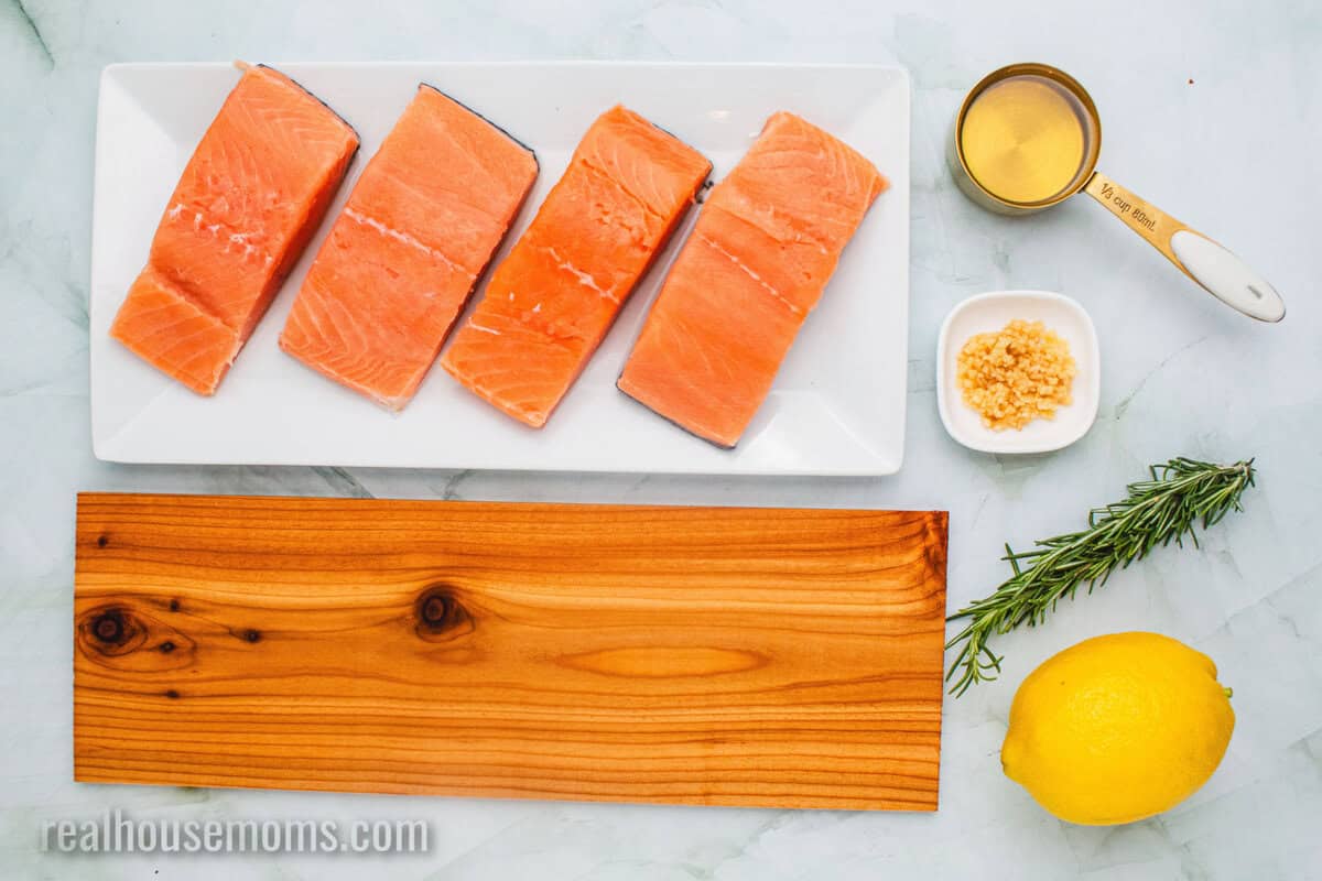 ingredients to make cedar plank salmon laid out next to a cedar plank on a counter