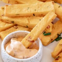 square image of cheddar bacon polenta fries on a plate with one dipped in chipotle aioli